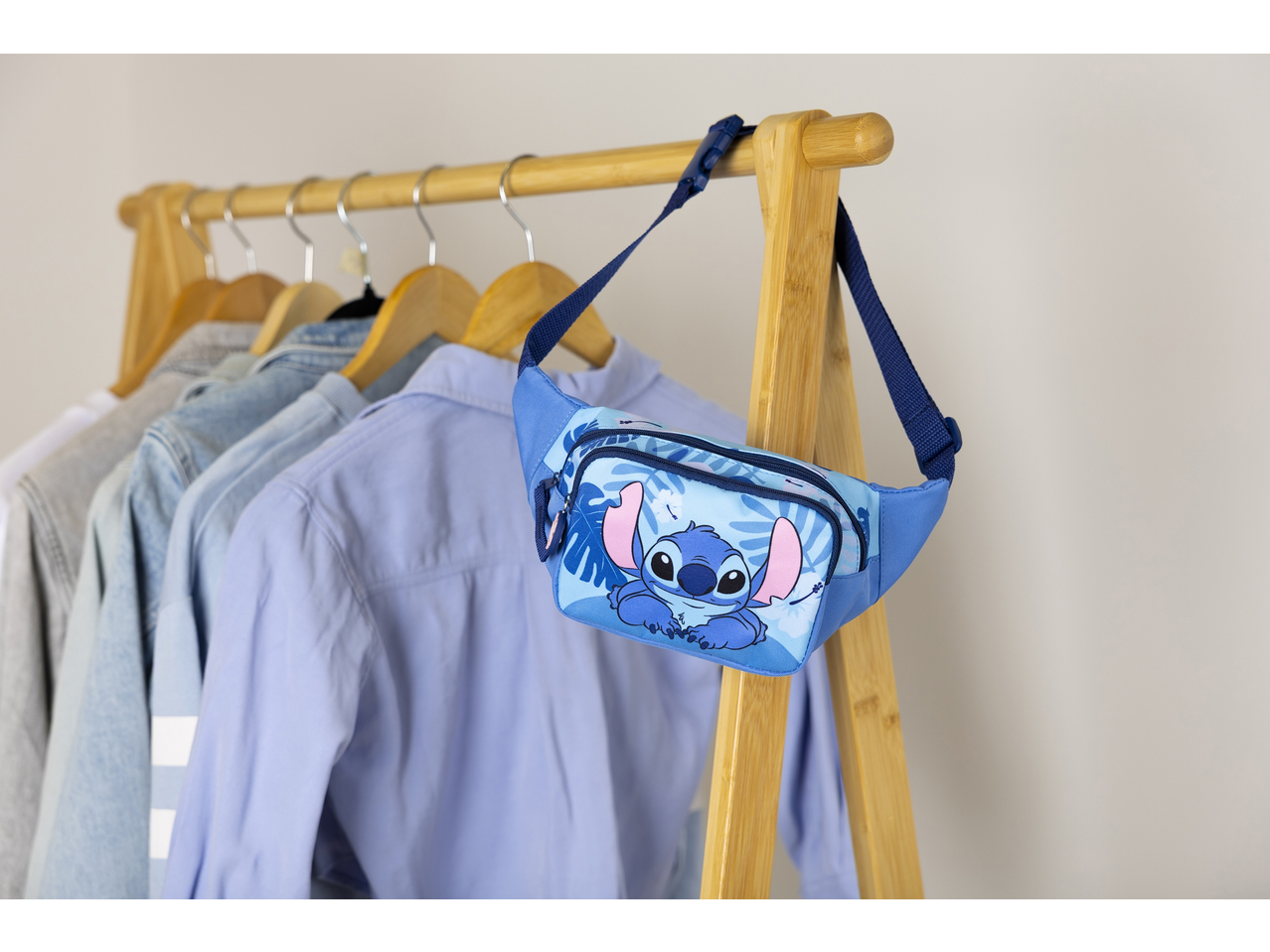 Bolsa de cintura azul com design do Stitch pendurada num cabide com camisas.