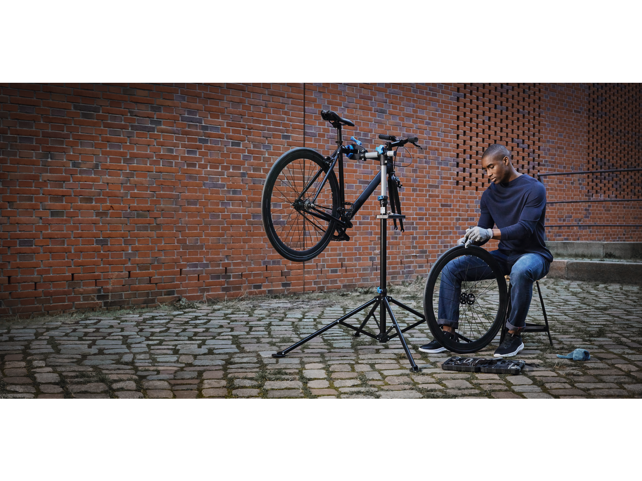 Man repairing a bicycle on a repair stand, holding a wheel, with tools nearby.