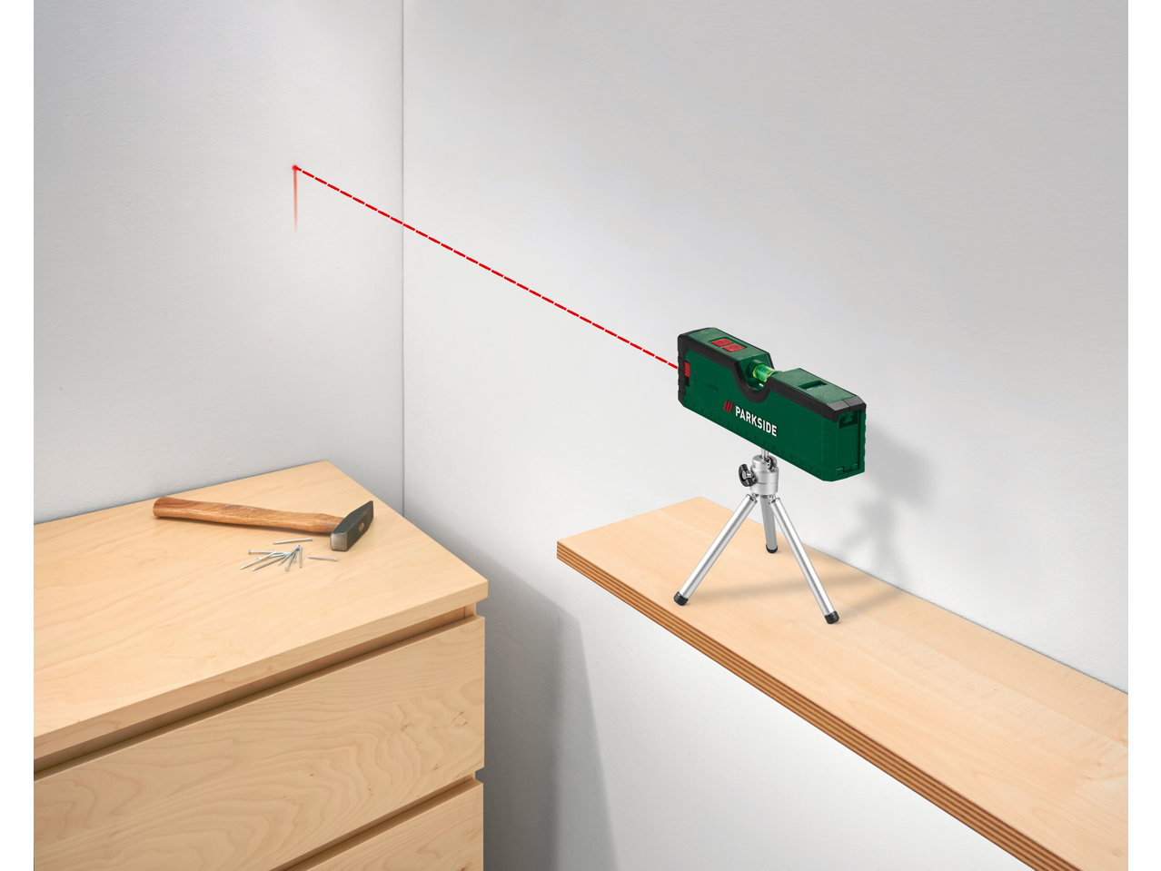 Nível a laser Parkside em tripé projetando uma linha vermelha na parede, com martelo e pregos.