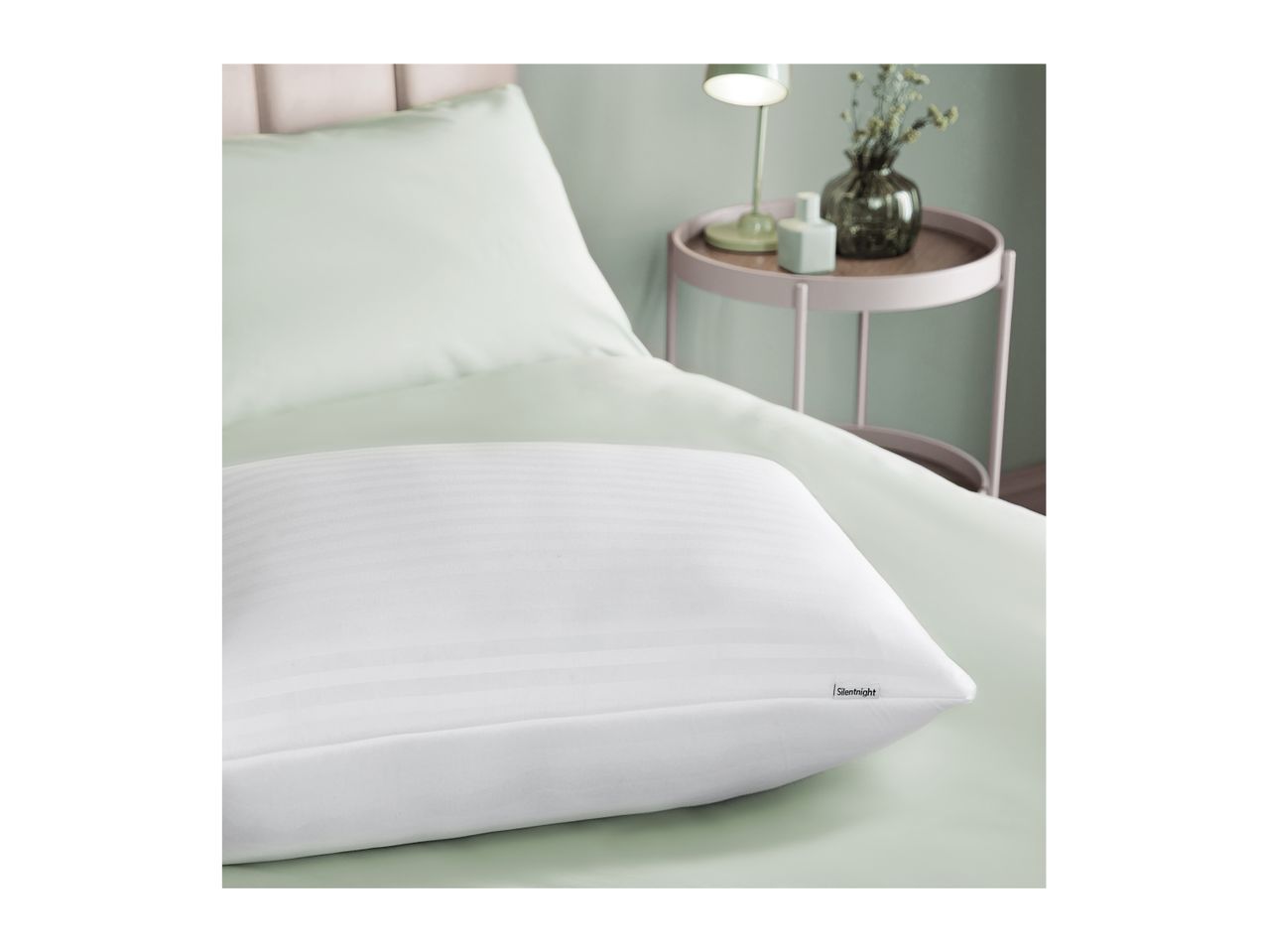 White striped pillow on a light green bed with a bedside table and lamp.