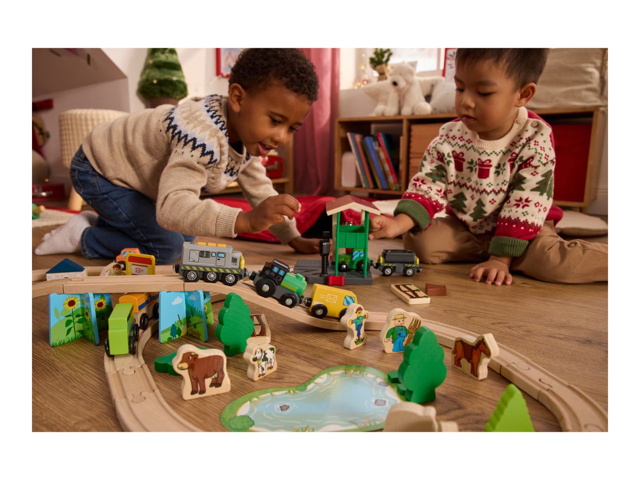 Two children playing with a wooden train set and farm animal figures.