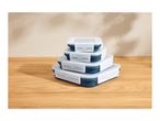 Stack of four rectangular food storage containers with blue bases and clear lids on a wooden surface.