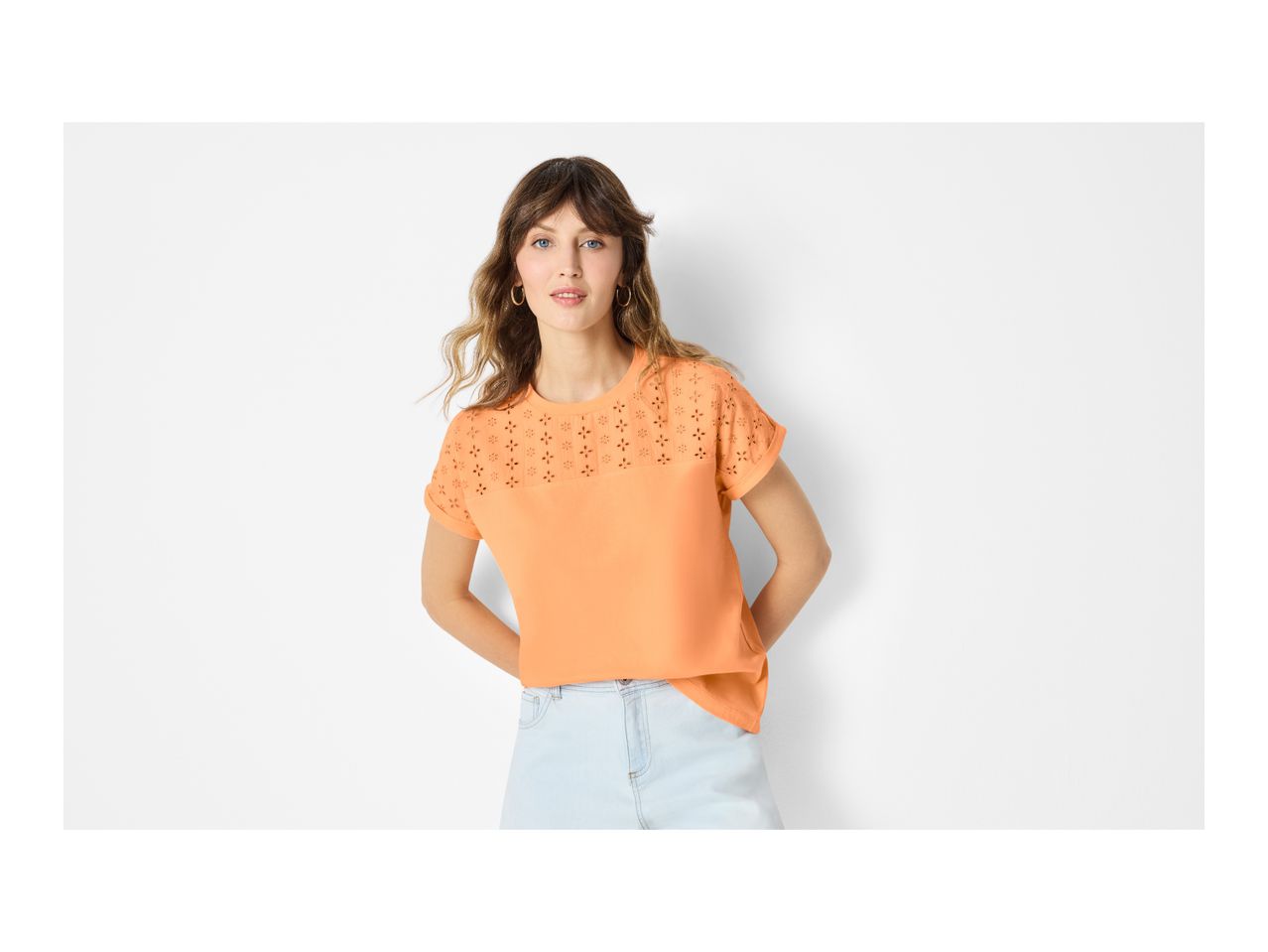 Woman in an orange short-sleeved top with eyelet embroidery and light blue denim shorts