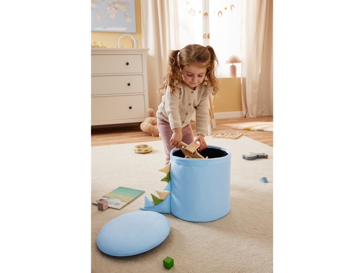 Menina brincando com brinquedos de madeira e caixa organizadora azul em formato de dinossauro.