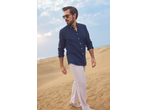 Man in a navy blue linen shirt and light trousers walking on sand dunes.