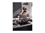 Woman cooking with two frying pans on an induction hob in a modern kitchen.
