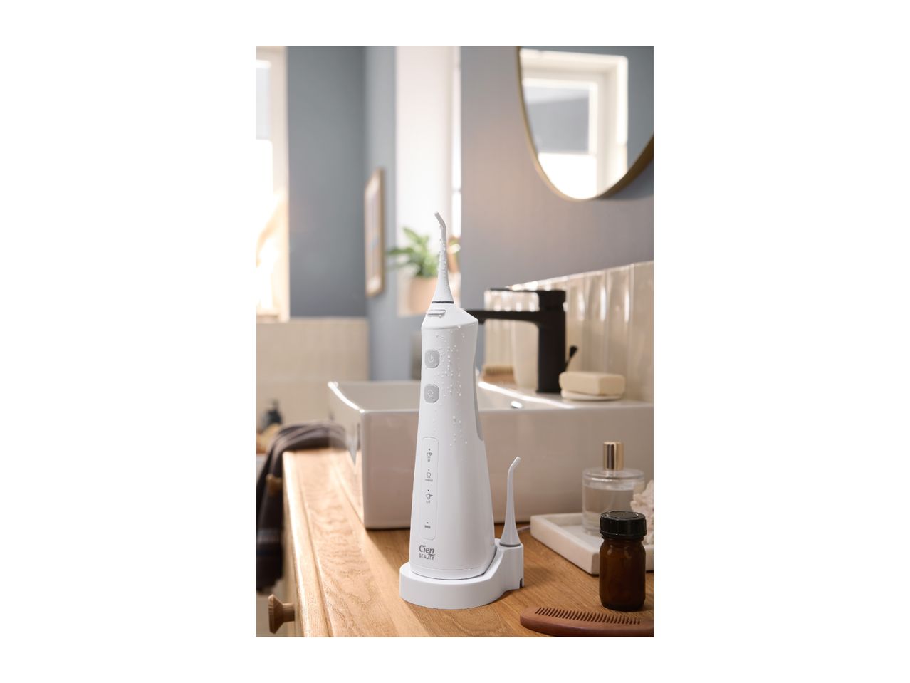 White oral irrigator with water droplets on a wooden bathroom counter with a sink.