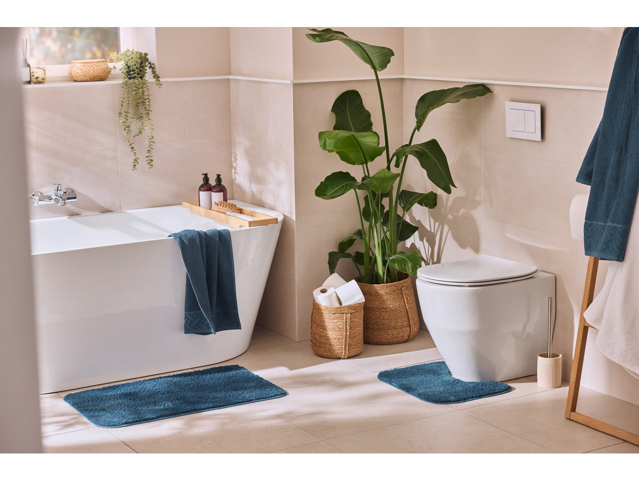 Baie cu covorașe de baie LIVARNO albastre, cadă, toaletă și plante.