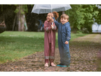 Doi copii în costume de ploaie și cizme sub o umbrelă, în ploaie.