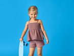 Smiling girl in a summer top and shorts, holding a blue skateboard.