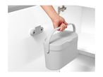 A hand lifting a grey, portable waste bin with a handle from its cabinet door mount.