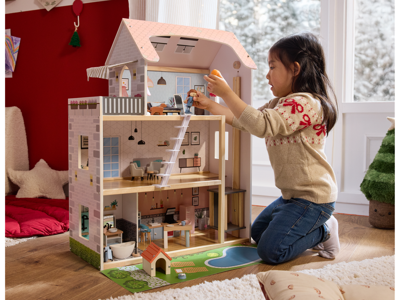 A child plays with a Lupilu wooden doll's house, featuring multiple rooms and accessories.