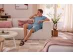 Man in blue polo shirt and shorts relaxing on a sofa in a bright living room.