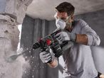 Man in safety gear using a cordless rotary hammer drill to break through a wall.