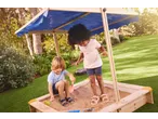 Two children playing in a wooden sandbox with a blue canopy, surrounded by green grass.