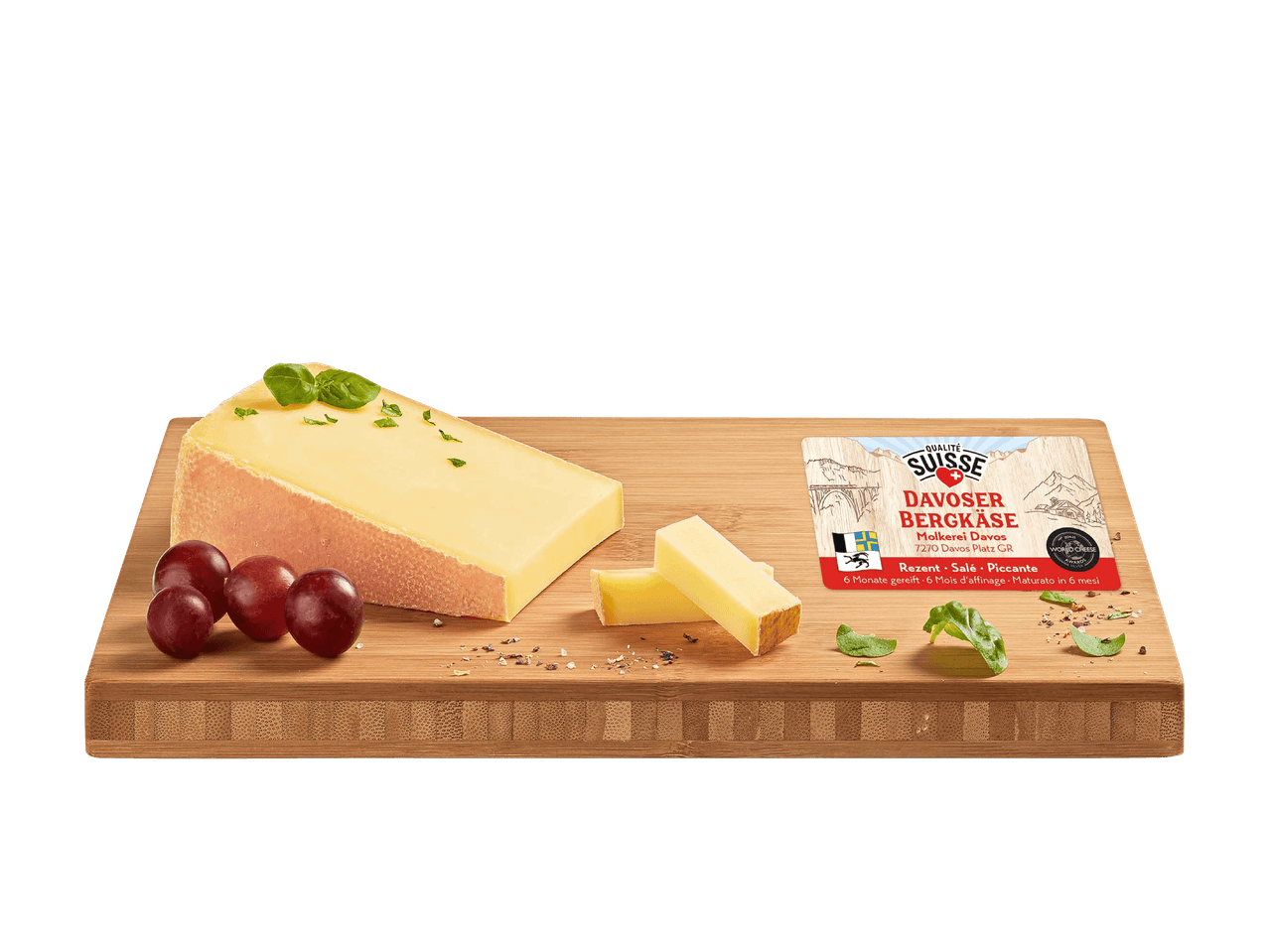 Schweizer Käse auf Holzbrett mit Trauben und Basilikum, Etikett sichtbar.