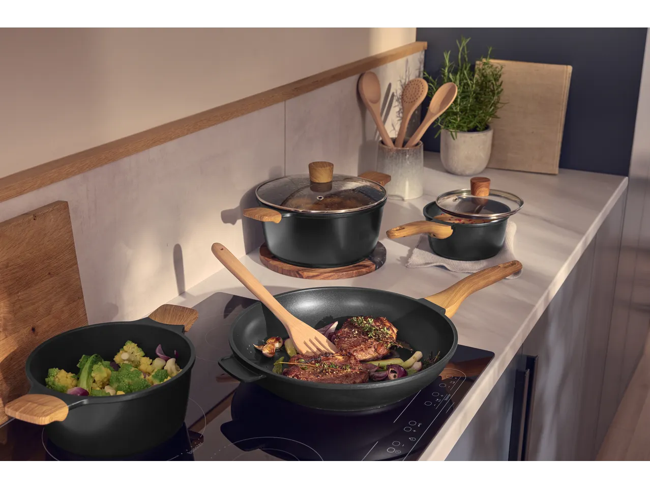 Panelas e frigideiras SILVERCREST pretas com cabos de madeira numa cozinha moderna.