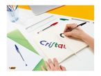 A person writing 'Cristal' in a notebook with colorful pens, surrounded by office supplies.