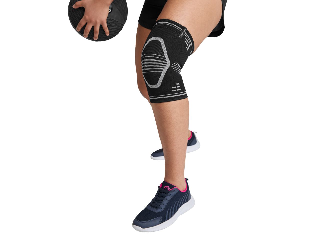 Person wearing a black knee brace and athletic shoes, holding a medicine ball.