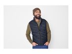 Man in a dark blue puffer vest, olive green sweater, and brown beanie smiling.