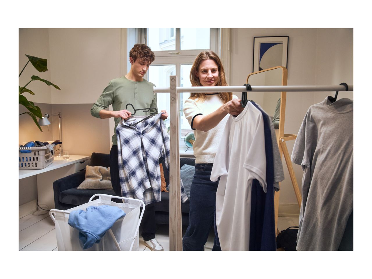 Two people hanging clothes on a rack, with a laundry basket nearby.