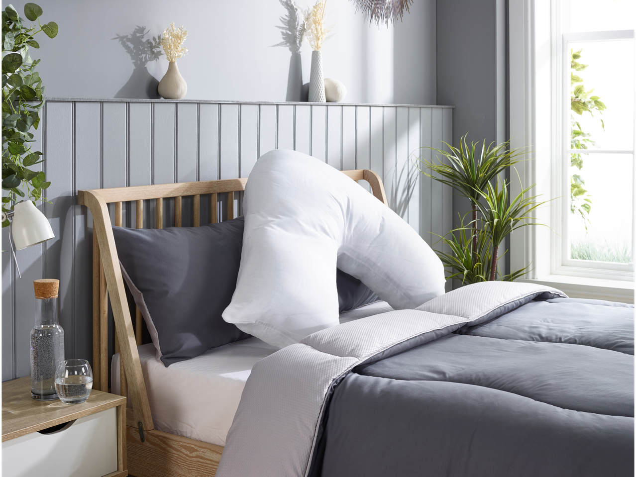 A U-shaped pregnancy pillow rests on a gray duvet-covered bed with gray and white bedding.