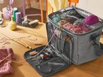 A gray yarn storage bag filled with colorful yarn and knitting supplies on a wooden table.