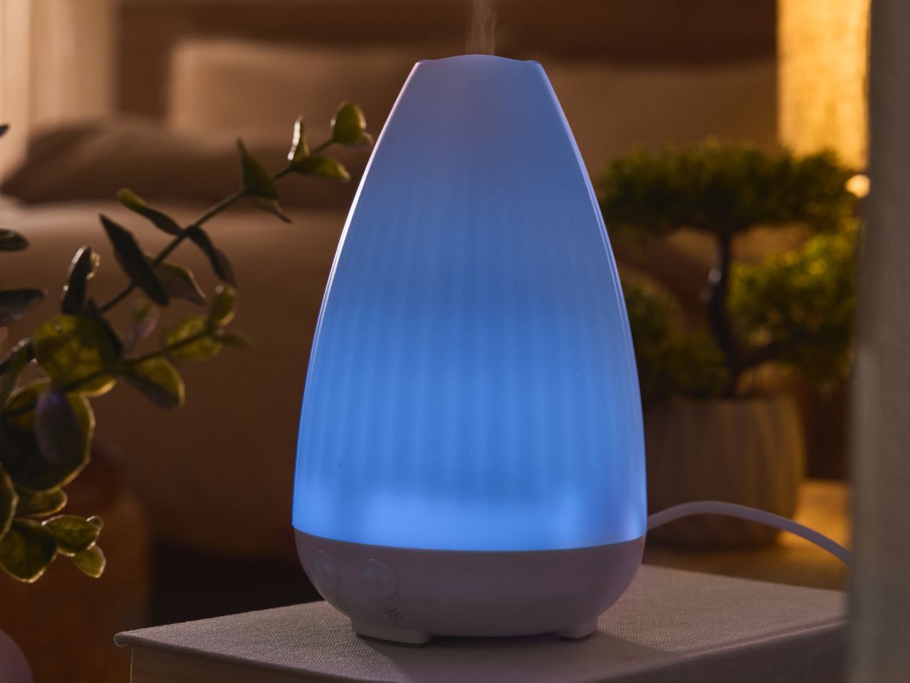 A blue-lit essential oil diffuser on a book in a dimly lit room.