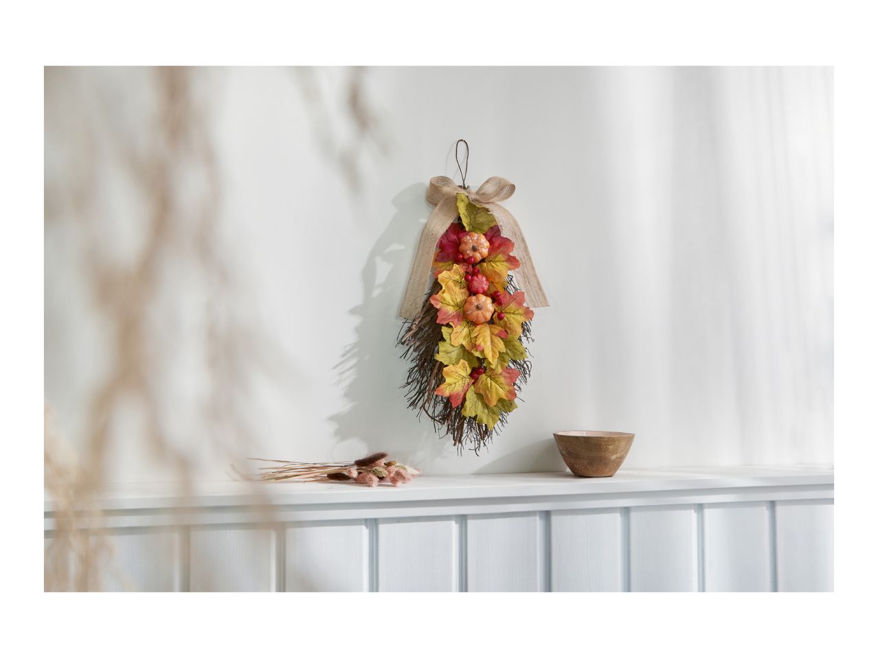 Autumnal door swag with pumpkins and leaves, dried flowers, and a wooden bowl on a shelf.