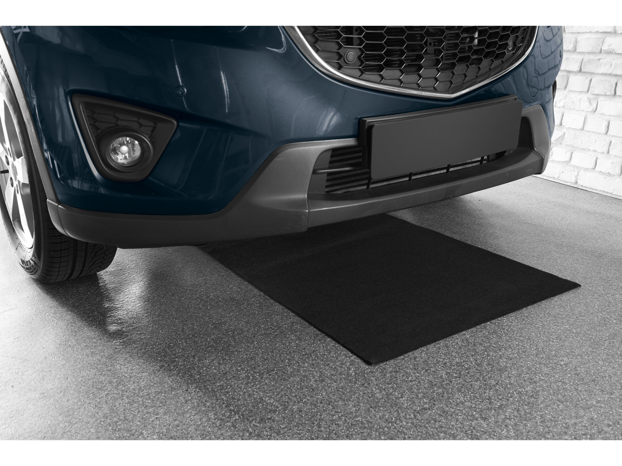 Car parked on a black garage mat, with a brick wall in the background.