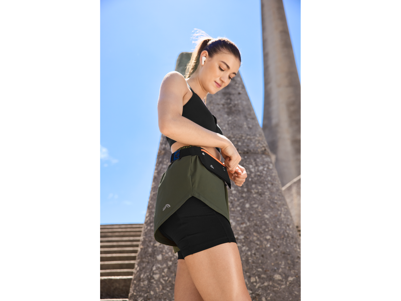 Mulher em roupa desportiva CRIVIT, a ajustar um cinto de corrida.