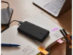 A TRONIC power bank charges a smartphone on a notebook next to a laptop and stationery.