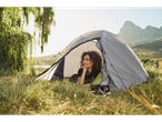 Uma mulher relaxa dentro de uma barraca de camping Coleman em um campo gramado.