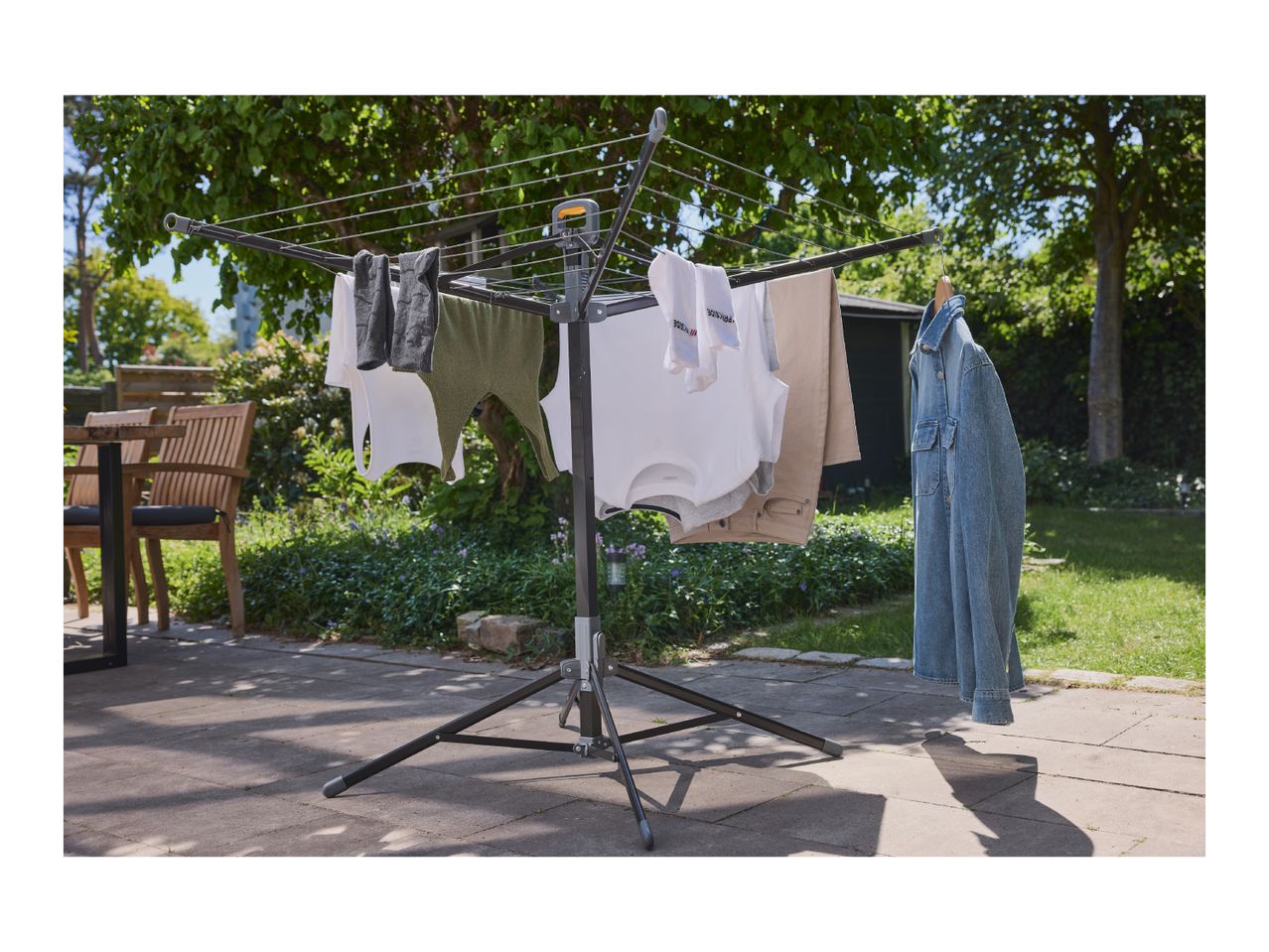Clothes drying rack with various clothes, including shirts, towels, and a denim jacket, outdoors.