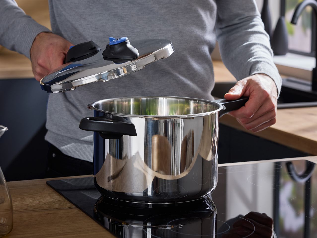 Man opening a pressure cooker on an induction hob in a modern kitchen.