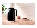 A black electric kettle on a wooden kitchen countertop next to cookies and a jar.