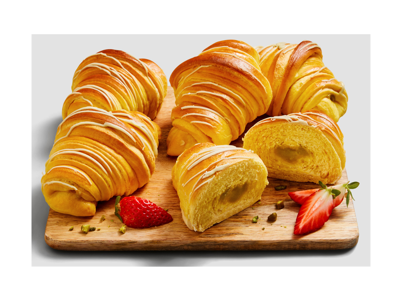 Pães doces com cobertura branca e recheio, servidos em uma tábua de madeira com morangos e pistaches.