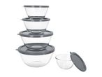 A stack of four clear glass mixing bowls with grey lids, and one smaller bowl with a lid beside them.