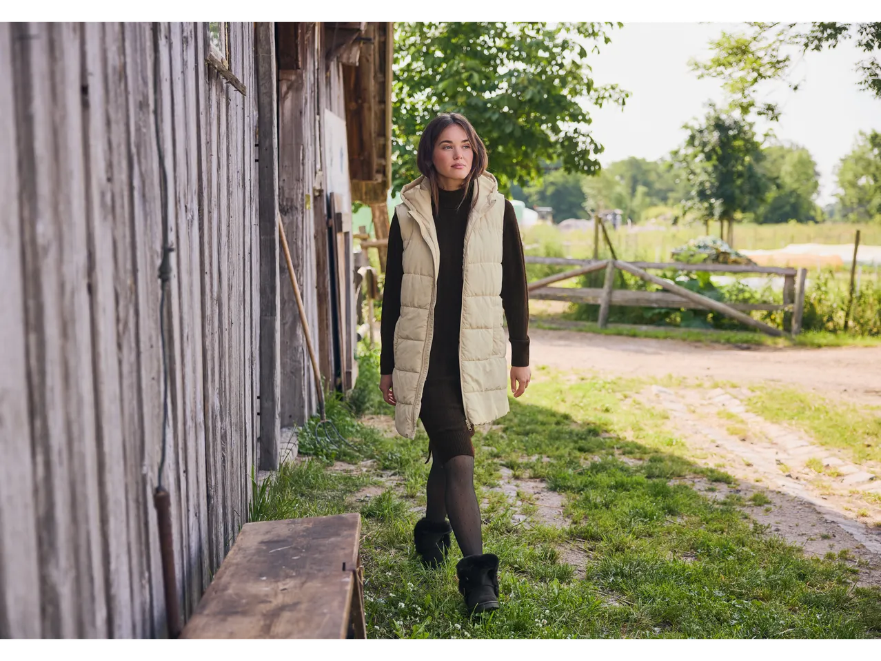 Woman in Esmara® dress and vest walking along a wooden wall.