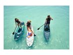 Three people paddleboarding on clear turquoise water, wearing life vests.