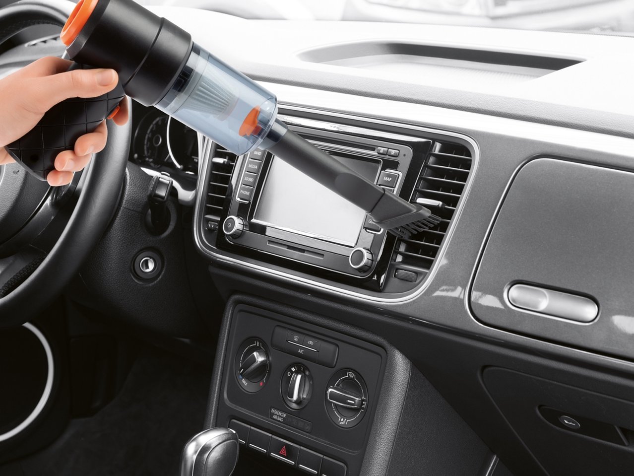 Ръчна прахосмукачка за кола, почистваща вентилационните отвори на таблото.