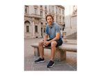 Man in a blue polo shirt, navy shorts, and sneakers sitting on a stone bench.