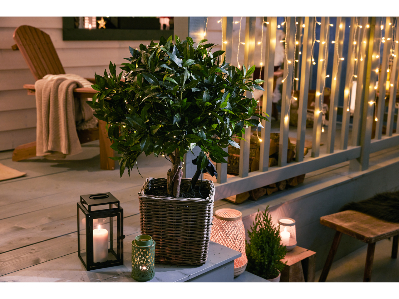 Luzes de corda exteriores iluminam um alpendre acolhedor com uma planta em vaso e lanternas.