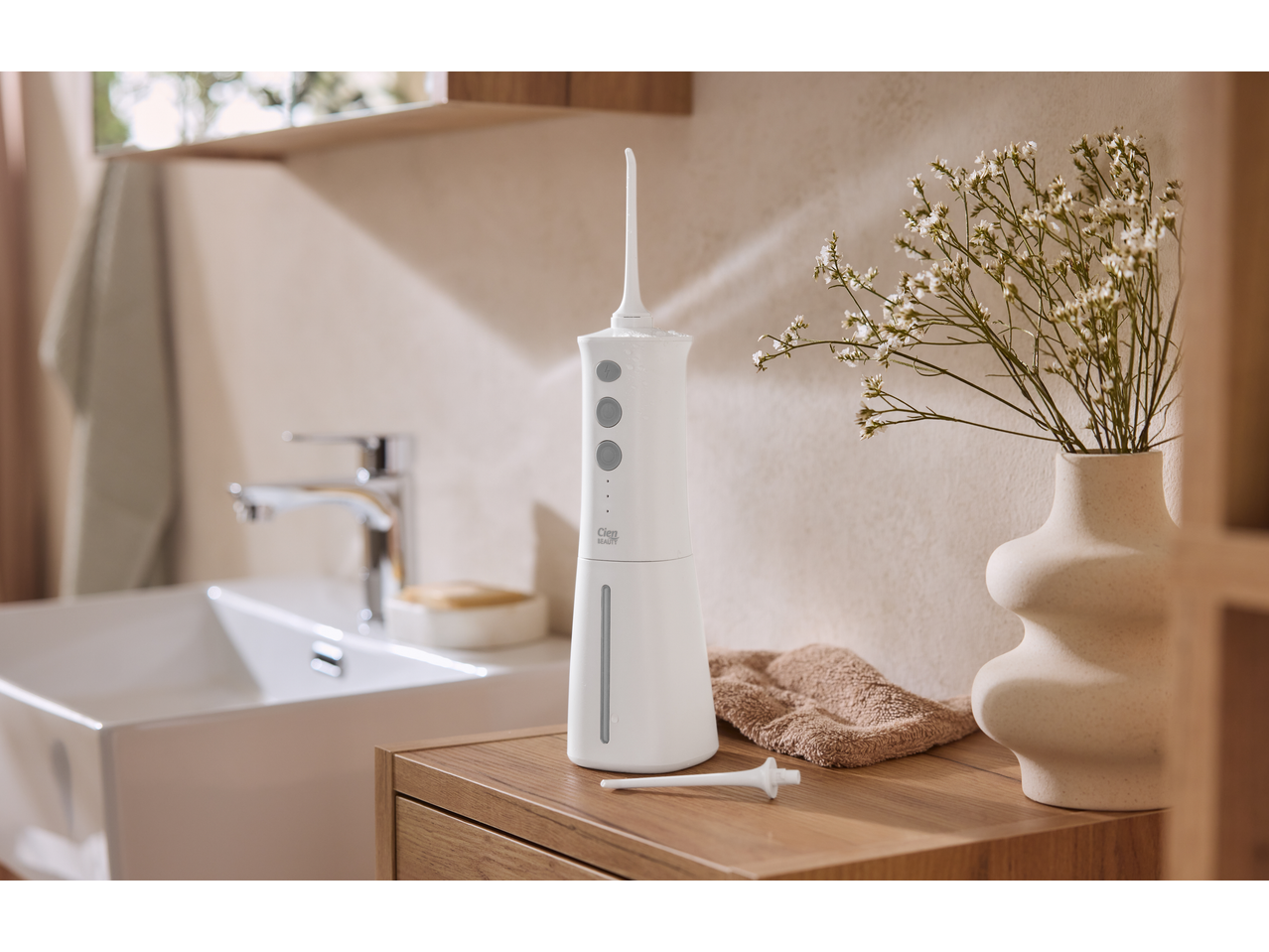 Duș bucal Cien Beauty pe un blat de baie din lemn, cu chiuvetă și flori.