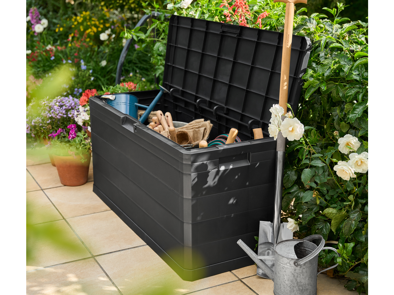 Livarno Garden Storage Box filled with gardening tools on a patio surrounded by flowers