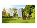Rotary clothesline with white laundry drying in a sunny garden with wooden patio furniture.