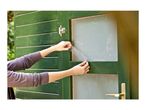 Hands applying privacy film to a window on a green wooden shed.