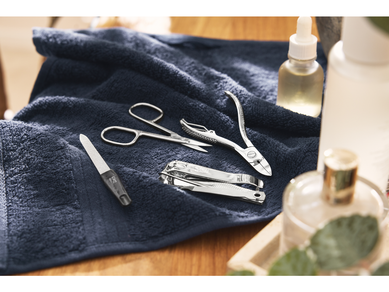 Ferramentas de manicure e pedicure, incluindo corta-unhas e tesouras, sobre uma toalha azul.