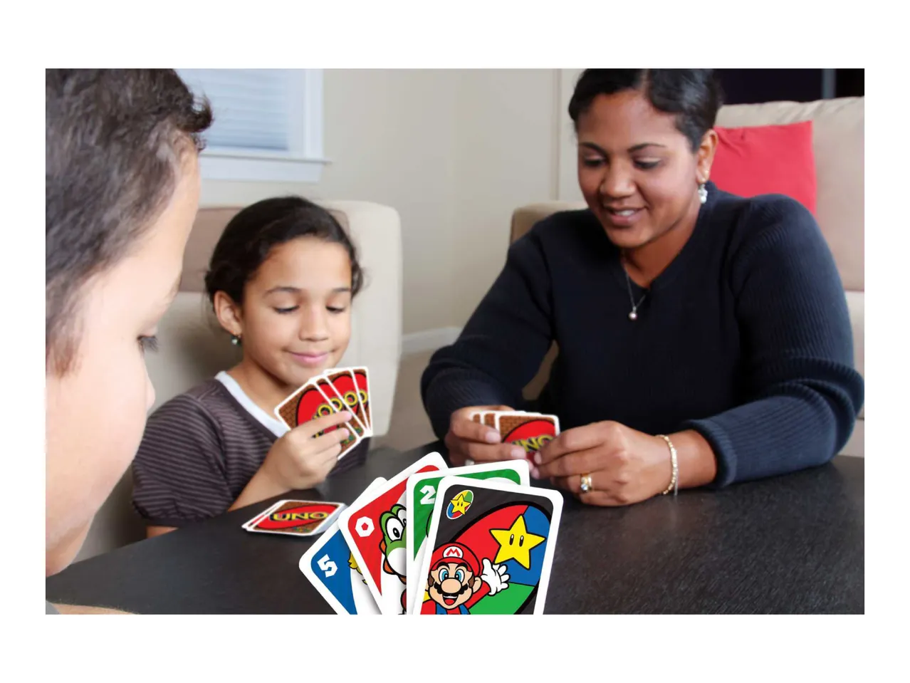 Family playing a card game at a table, with various cards visible.