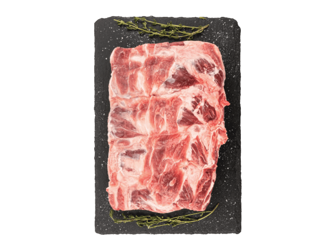 Šviežia kiaulienos šonkaulių juosta su rozmarinais ir druska ant juodos lentos.